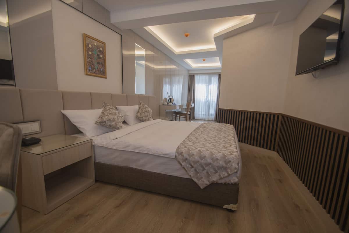 Ein modernes Hotelzimmer mit einem großen Bett, Nachttischen, einem Schreibtisch und einem an der Wand befestigten Fernseher.