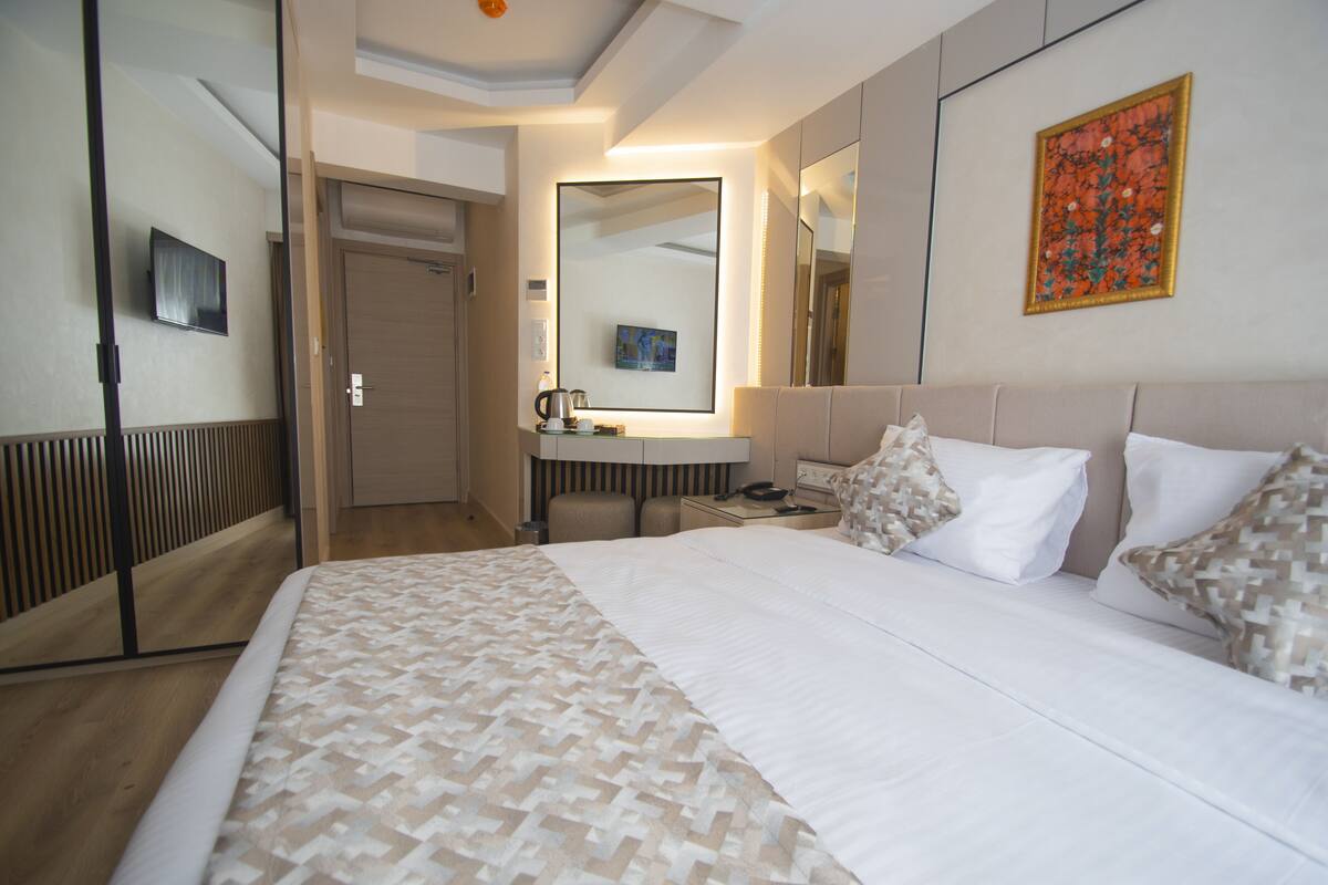 Ein Hotelzimmer mit einem großen Bett, einem Nachttisch, einem Spiegel und einem an der Wand befestigten Fernseher.