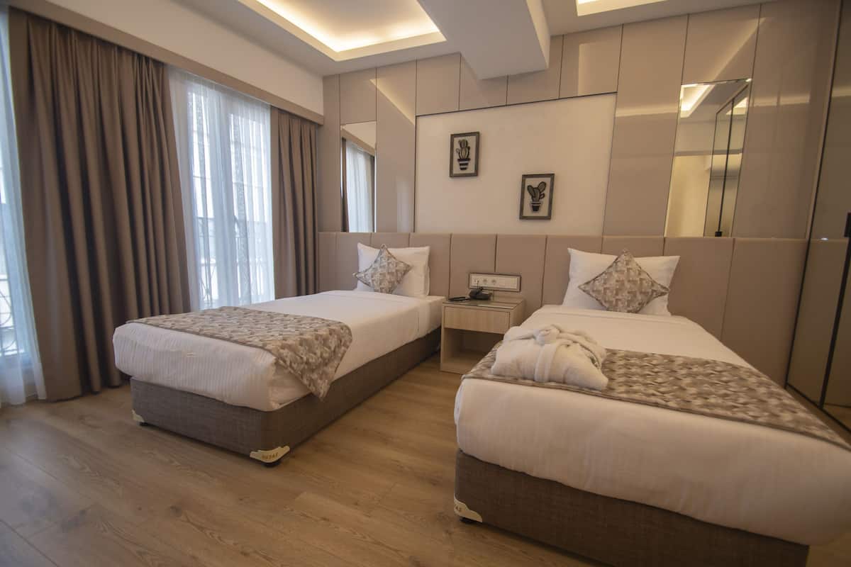 Ein Hotelzimmer mit zwei Betten, einem Nachttisch und einem großen Fenster mit Vorhängen.