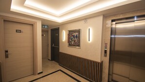 Un couloir d’hôtel moderne avec un ascenseur, une porte portant l’inscription « 304 » et une œuvre d’art encadrée accrochée au mur.