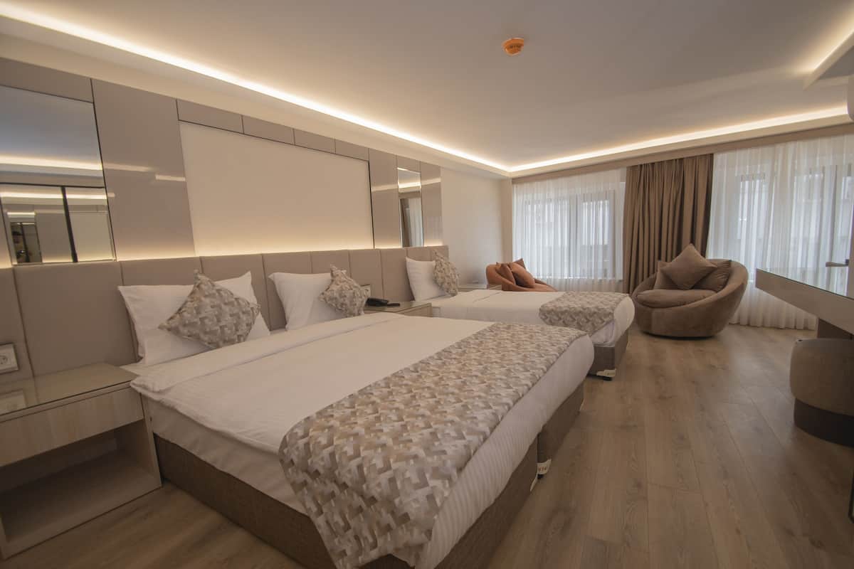 Ein modernes Hotelzimmer mit zwei Betten, einer Sitzecke und einem großen Fenster mit Vorhängen.