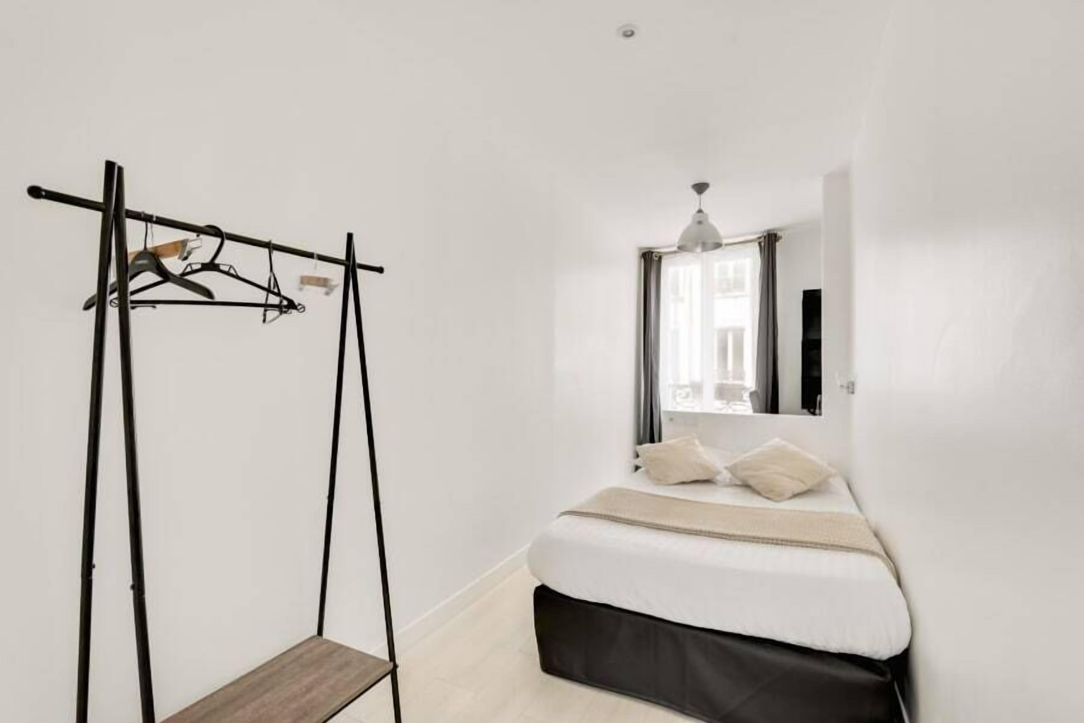 A minimalist bedroom with a bed, a hanging clothes rack, and a small wooden bench.