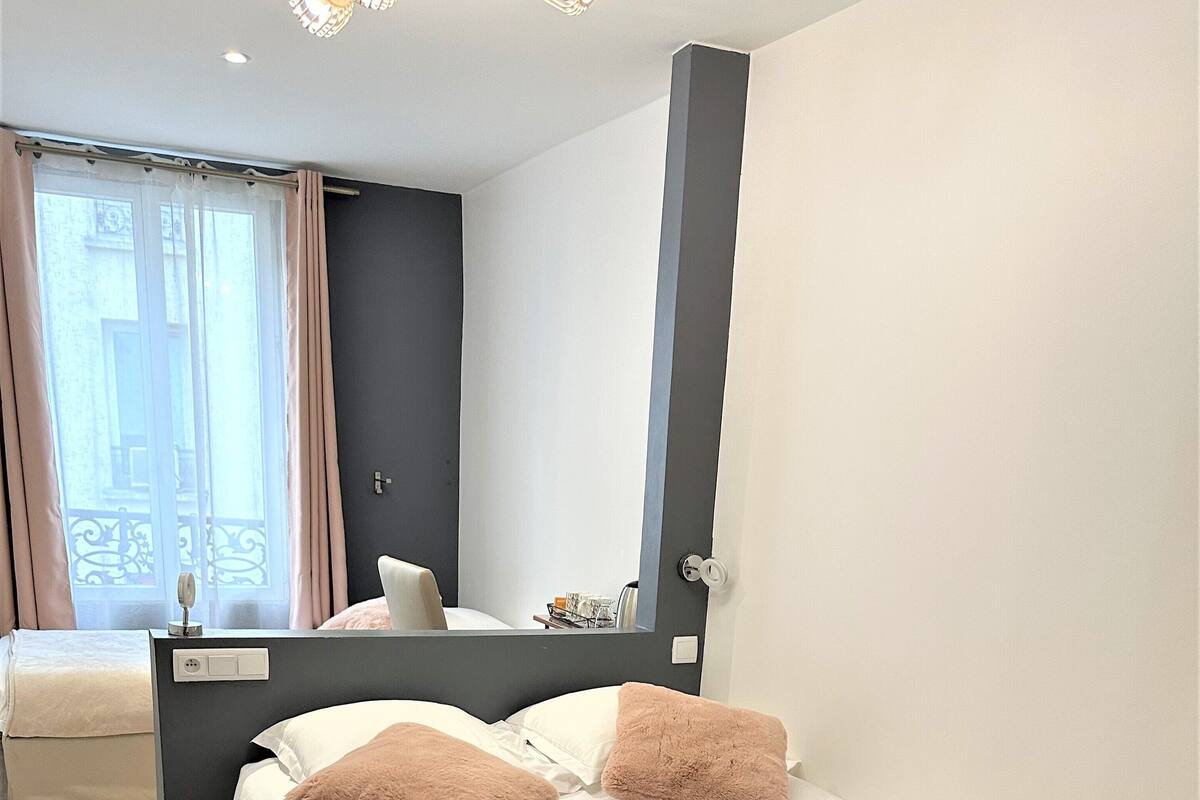 A hotel room with a bed, a bedside table, a mirror, and a window with curtains.