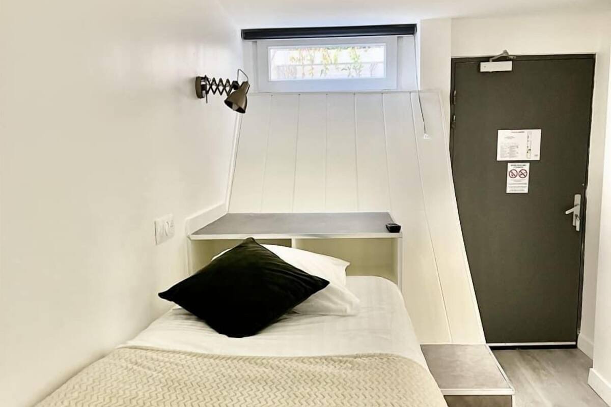 A bedroom with a bed, a window, a door, and a staircase.
