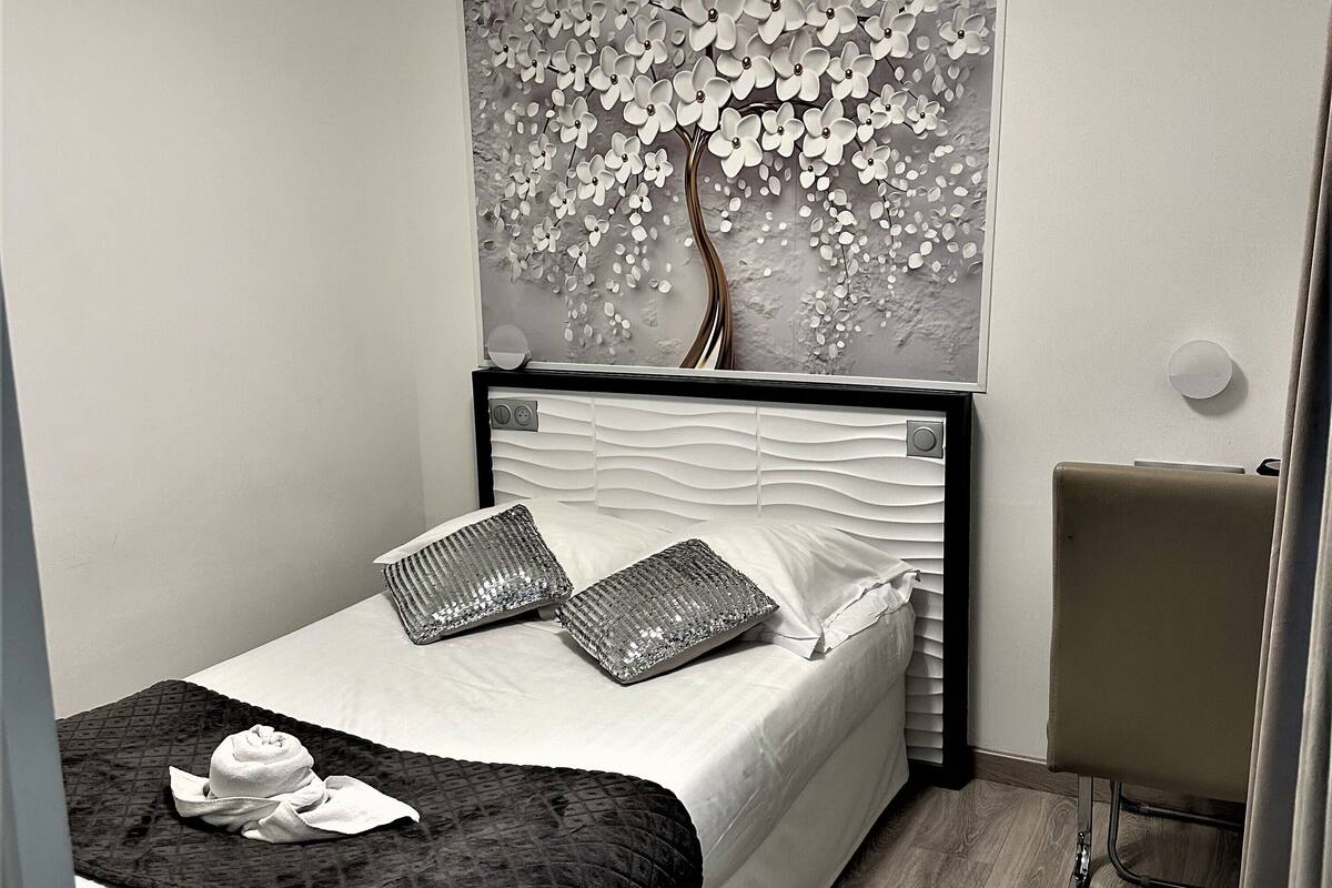 A neatly arranged bedroom with a bed, pillows, a bedside table, and a wall-mounted artwork.