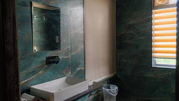 A bathroom with a marble wall, a white sink, a mirror, and a window with blinds.