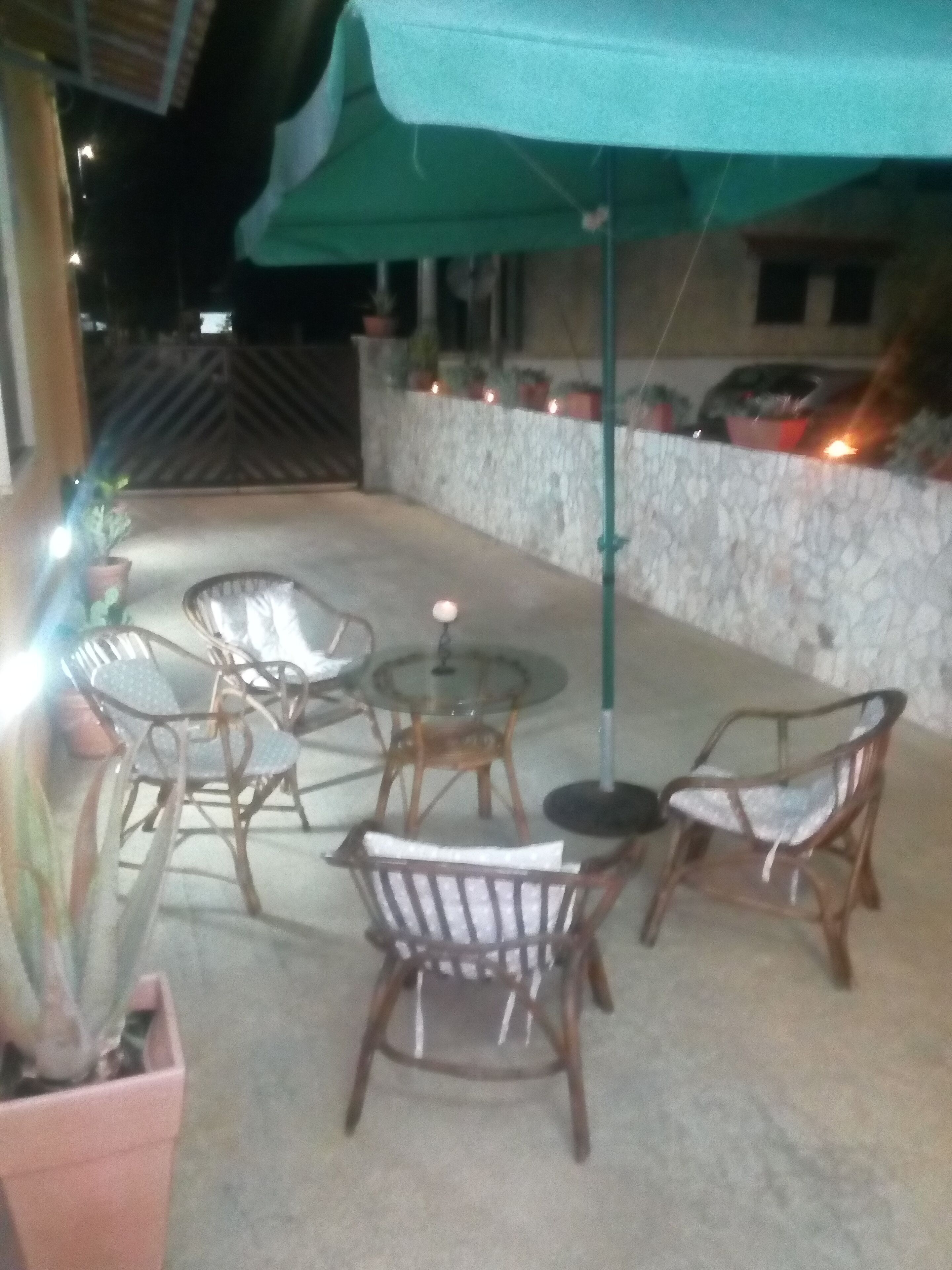Un patio al aire libre con mobiliario de mimbre, una mesa de vidrio y un paraguas verde.