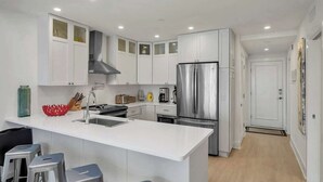 A modern kitchen with white cabinets, a stainless steel refrigerator, and a central island with bar stools.