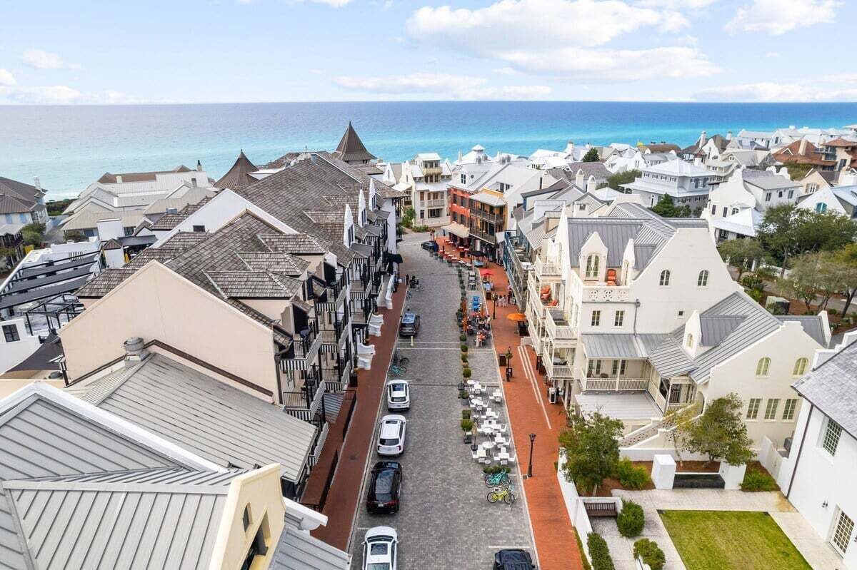 A coastal town with narrow streets lined with buildings, a clear view of the sea, and parked cars along the road.