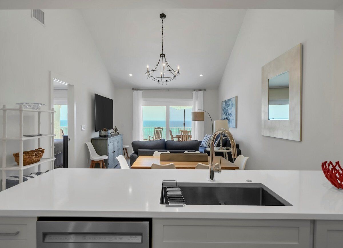 Una cocina moderna con una isla central, una zona de comedor con sofá y sillones, y vista al mar a través de amplios ventanales.