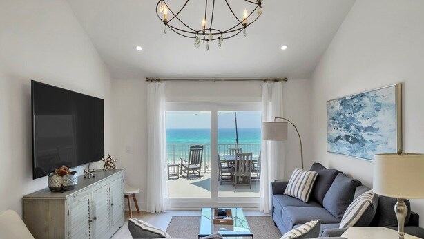 A modern living room with a large TV, a sofa, a coffee table, and a view of the ocean through large sliding doors.