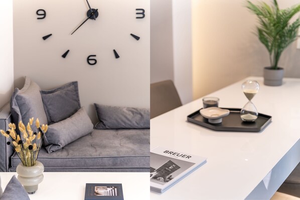 A modern living room with a grey sofa, a wall clock, and a vase with dried flowers. - Elegant 2BR Apartment in Kolonaki (Athens)