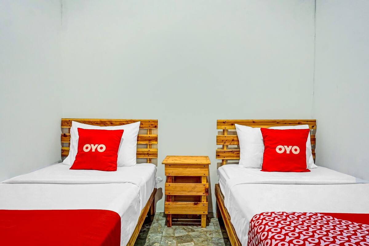 A room with two beds, each with a wooden headboard and a red pillow with the word "OYO".