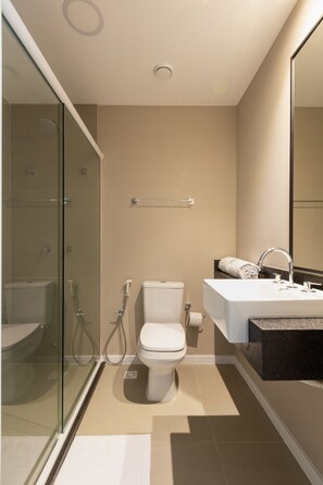 Une salle de bain moderne avec une douche à parois de verre, des toilettes blanches, un lavabo doté d’un plan de travail en marbre et un grand miroir.