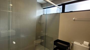 Un baño moderno con cabina de ducha de vidrio, un inodoro y un pequeño carro negro.