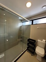 Un bagno moderno con box doccia in vetro, un water e un piccolo carrello nero.