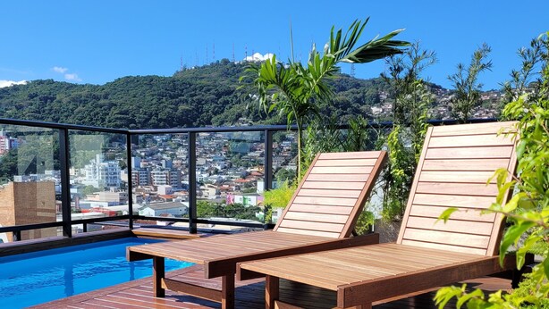A wooden deck with lounge chairs overlooking a swimming pool and a cityscape. - Bewiki (Florianópolis)