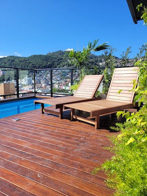 Une terrasse en bois avec des chaises longues donnant sur une piscine et sur le paysage urbain.