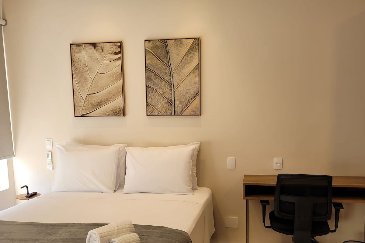 A hotel room with a bed, a desk, a chair, and two wall art pieces.