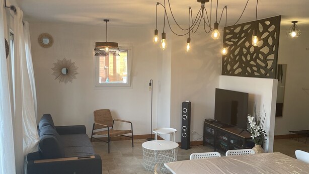 A modern living room with a sectional sofa, a dining table with chairs, a TV, and a decorative wall panel. - 2 steps from the lake. (Parentis-en-Born)