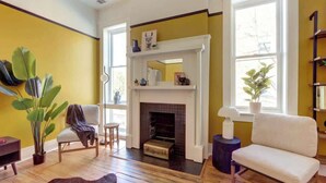 A living room with a fireplace, a sofa, a chair, a potted plant, and a wooden floor. - Carolina Gold @ The Huntingdon Lofts Collection (Savannah)