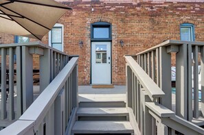 A staircase leading to a door with a small porch area, a brick building with a window and a door, and a metal railing on the left. - Carolina Gold @ The Huntingdon Lofts Collection (Savannah)
