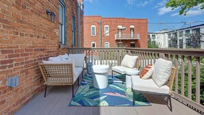 A balcony with a brick wall, a wicker chair, a white sofa, and a patterned rug. - Carolina Gold @ The Huntingdon Lofts Collection (Savannah)