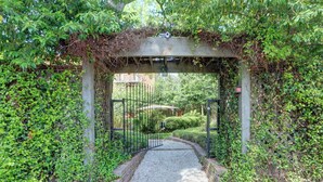 A gated entrance with a gravel path leading through a lush, vine-covered archway. - Carolina Gold @ The Huntingdon Lofts Collection (Savannah)