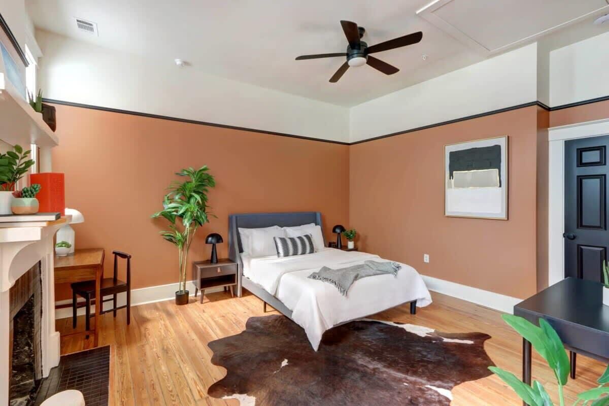 Un dormitorio moderno con cama, ventilador de techo, chimenea y alfombra de cuero de vaca.