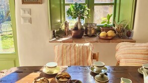 Ein Esszimmer mit gedecktem Tisch, verschiedenen Geschirr, einem Blumentopf und Blick ins Grüne.