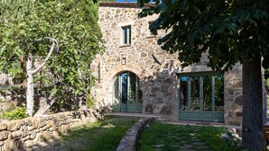 Ein steinernes Gebäude mit grüner Tür und Fenstern, umgeben von Bäumen und einem Steinweg.