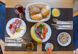 A breakfast setting with plates of food, a basket of bread, a glass of juice, and a bowl of cereal. - Strandhotel Seestern (Ostseebad Baabe)