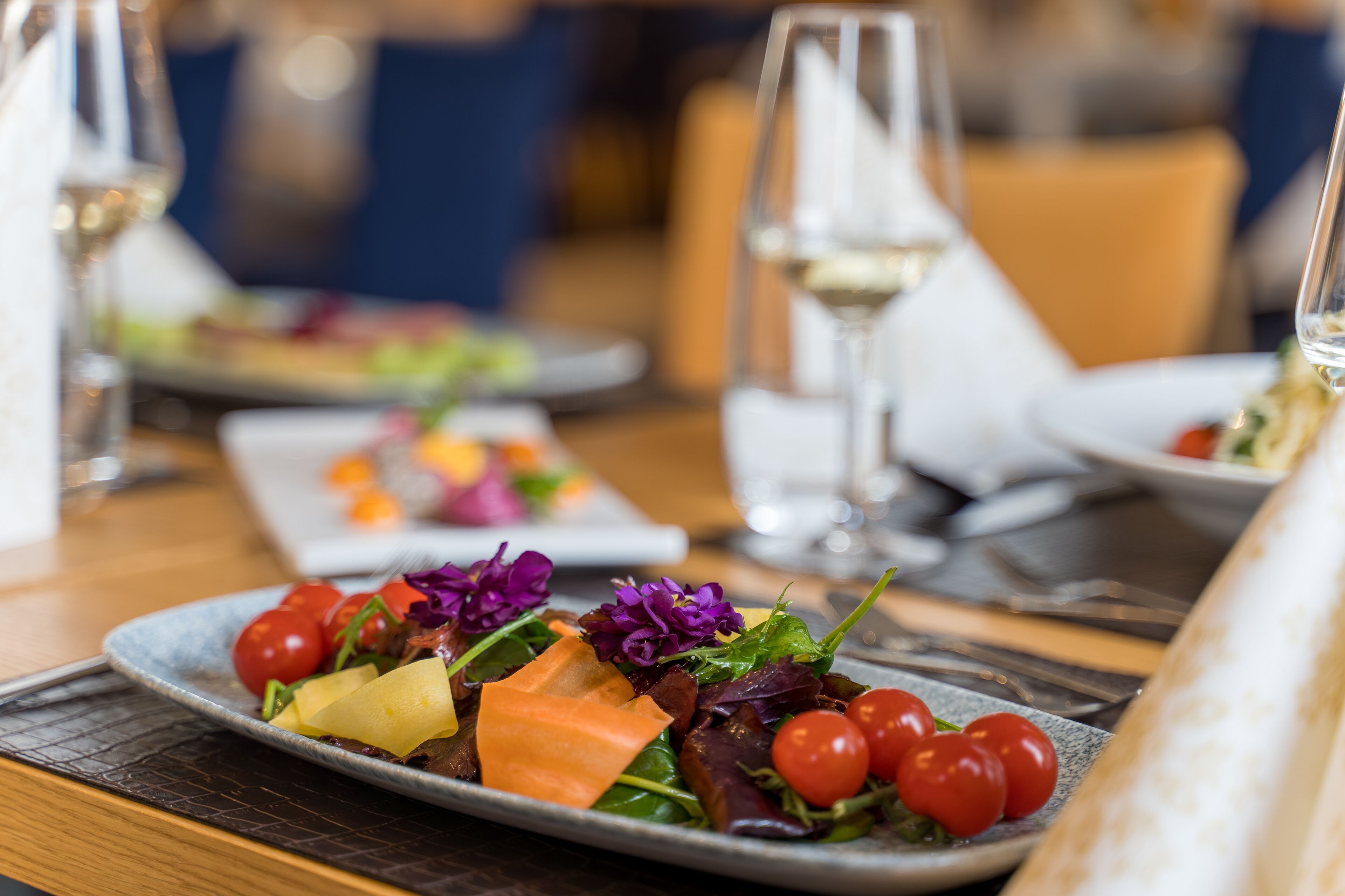 Una mesa de comedor con platos de comida, copas de vino blanco y una servilleta.