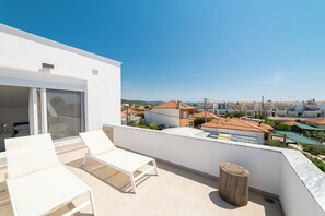 Eine Dachterrasse mit weißen Lounge-Stühlen, einem Holzschemel und Blick auf die Stadtlandschaft.