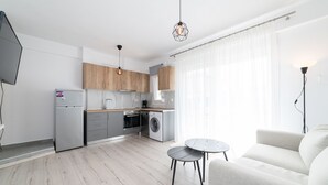 Eine moderne Küche mit Holzausstattung, einem eingebauten Backofen und einer Waschmaschine. Im Wohnbereich befindet sich ein runder Tisch und ein Sofa.