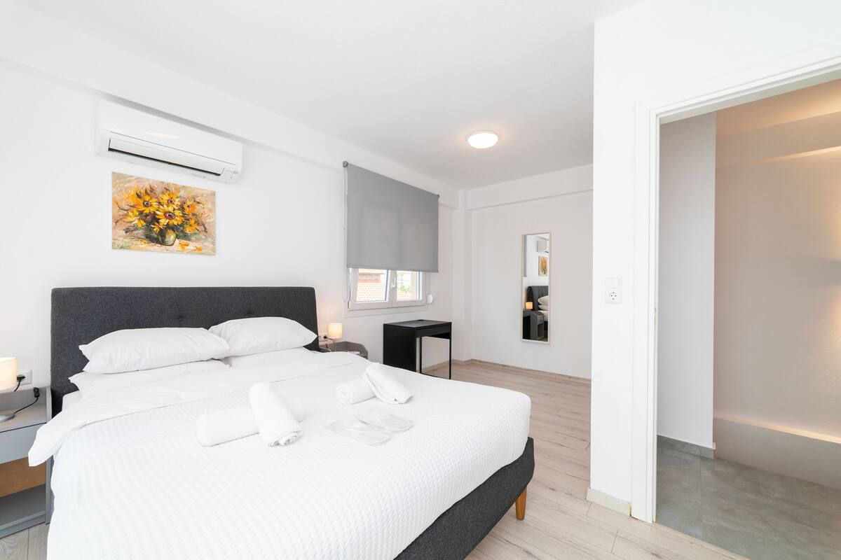 Ein modernes Hotelzimmer mit einem großen Bett, einem Nachttisch, einer Klimaanlage, einem Bild an der Wand und einem Fenster.