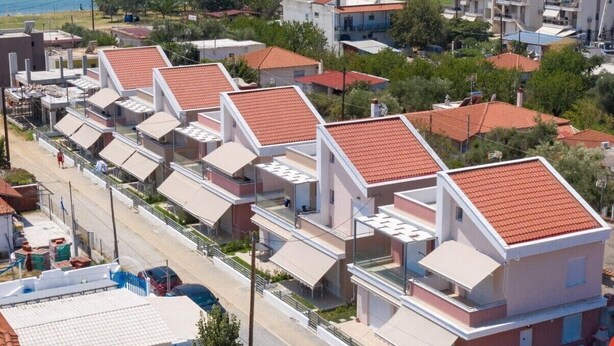 Ein Küstenwohngebiet mit modernen Gebäuden, freiem Blick auf das Meer und einer Straße mit geparkten Autos.