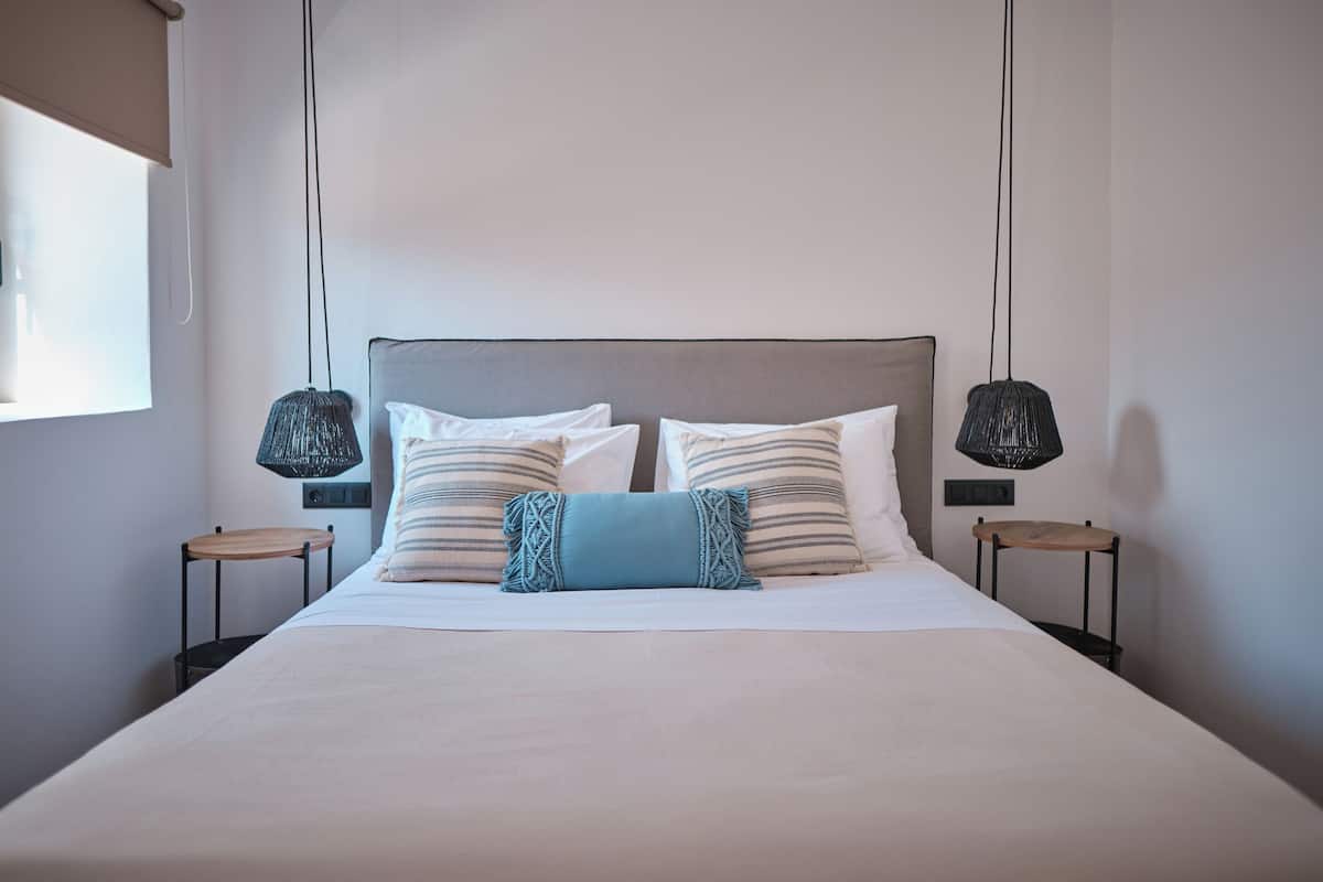 A neatly made bed with a grey headboard, two bedside tables with lamps, and a window on the left.