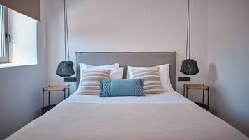 A neatly made bed with a grey headboard, two bedside tables with lamps, and a window on the left.