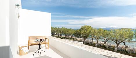 A balcony with a table and chairs, overlooking a beach with trees and the sea.