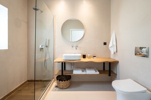 A modern bathroom with a glass shower enclosure, a round mirror, a wooden vanity, and a white toilet. - Eden Kythira (Kithira)