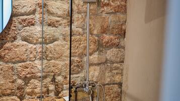A bathroom with a stone wall, a shower, and a mirror.
