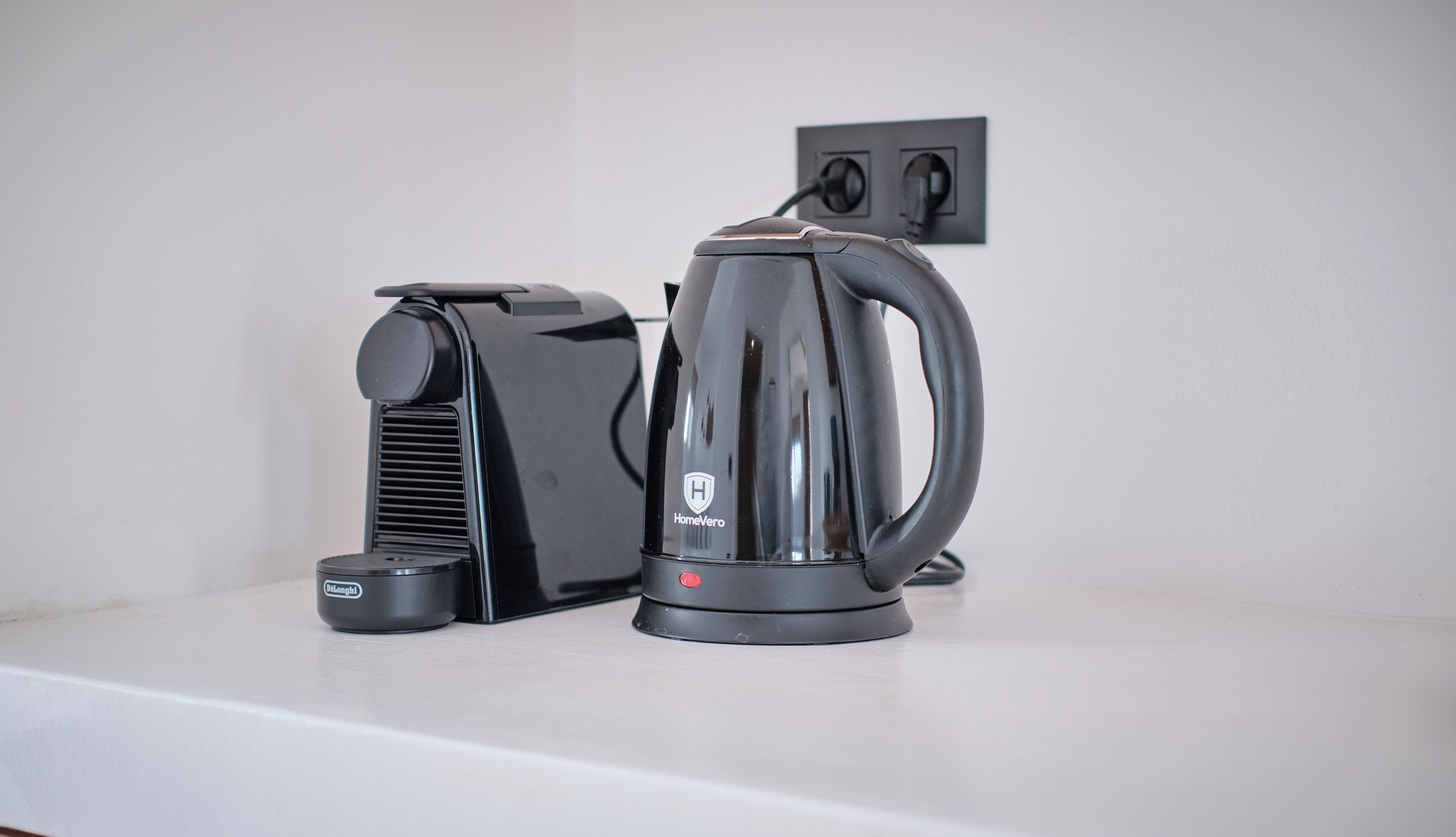 A black coffee maker and a black electric kettle on a white countertop.