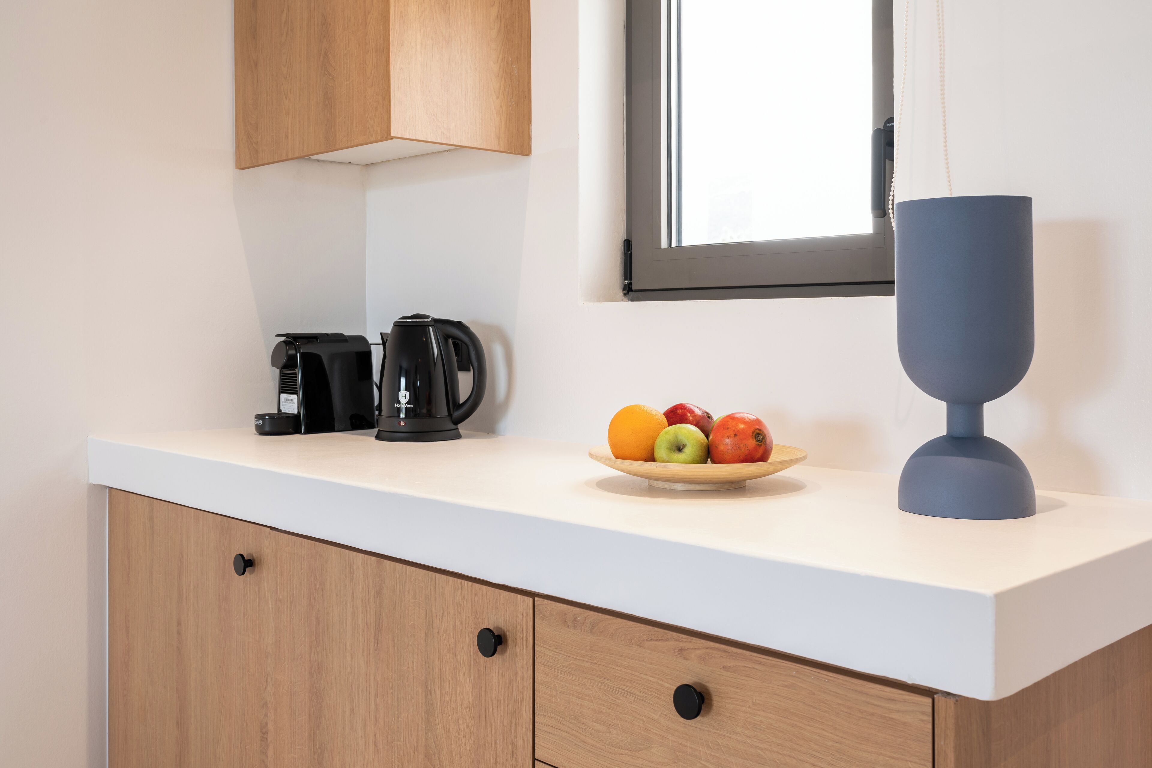 Una encimera de cocina con cafetera, hervidor y frutero.