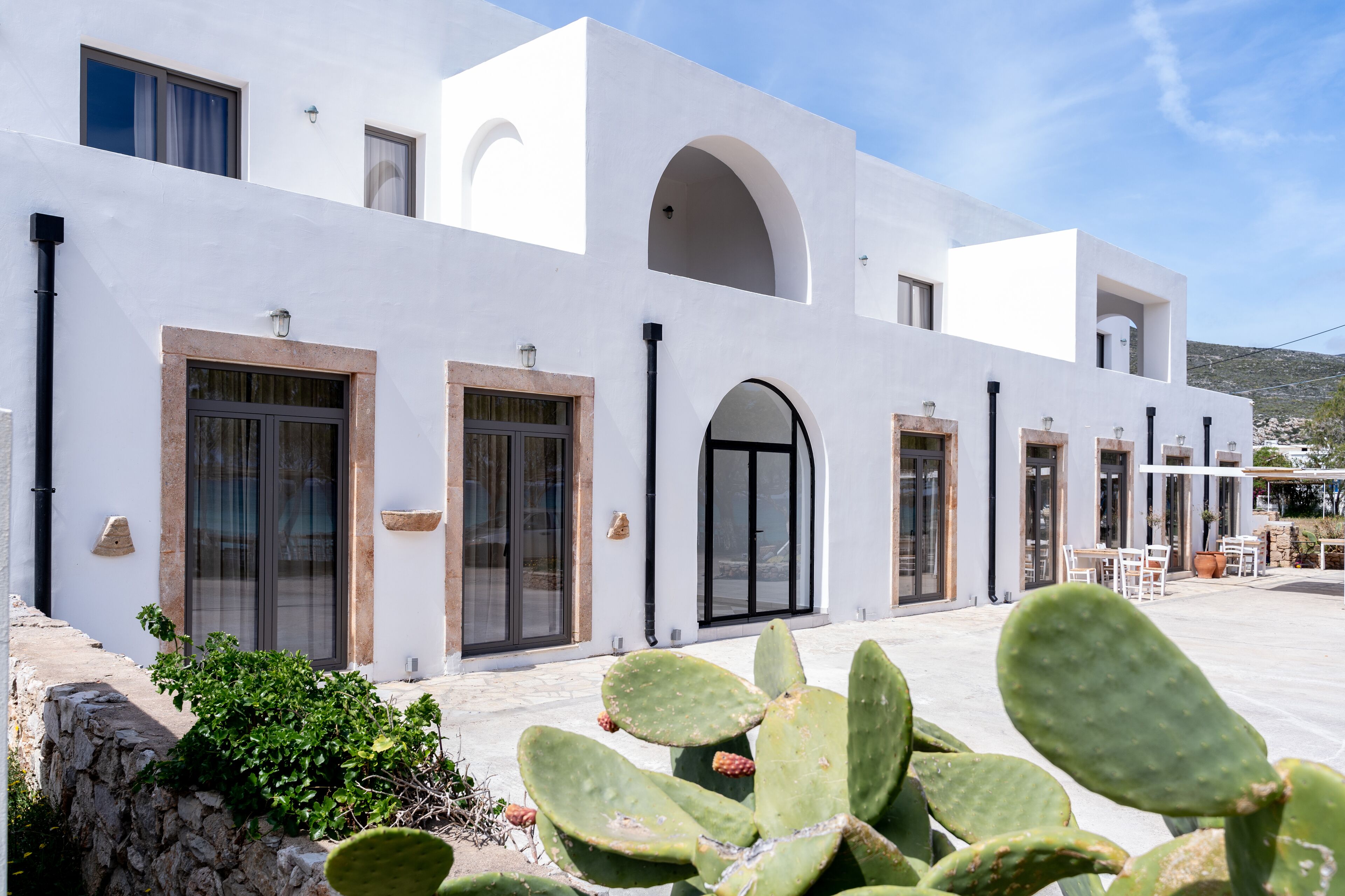 A white building with multiple doors and windows, a stone wall, and a cactus in the foreground.
