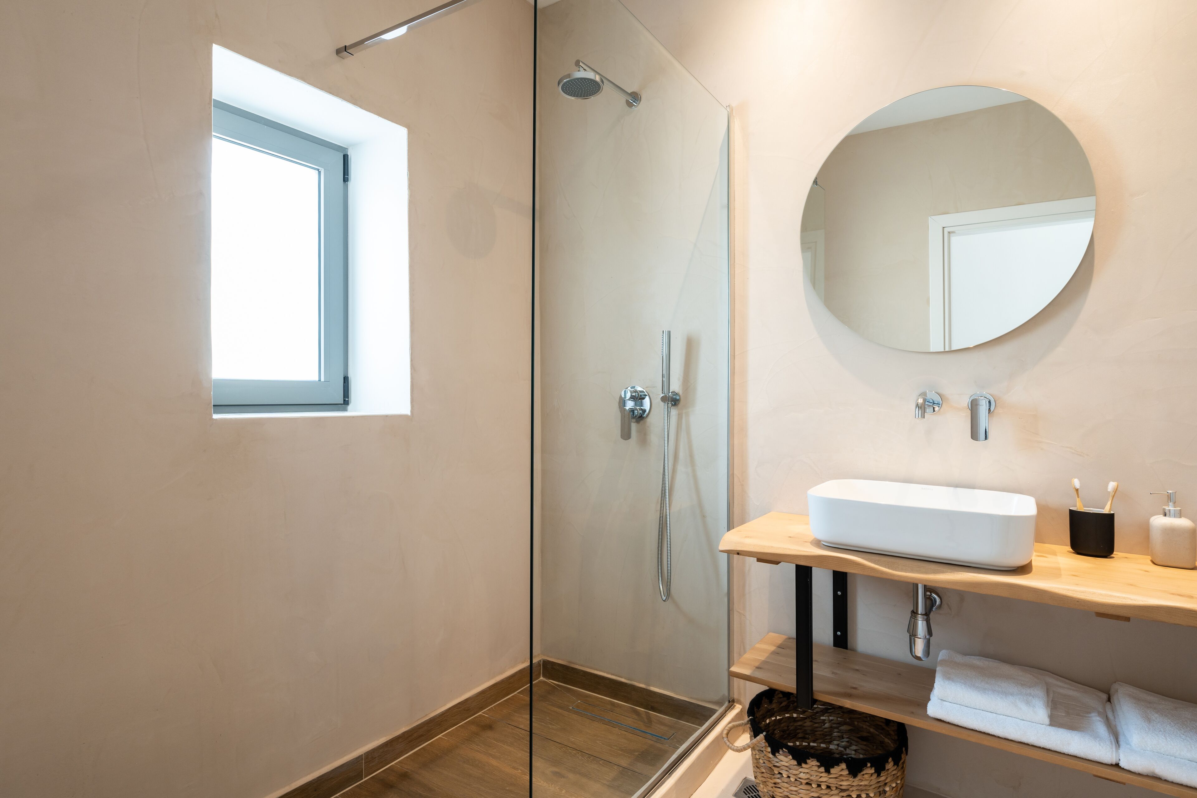 Un baño moderno con ducha envuelta en vidrio, un espejo grande y un tocador de madera con lavabo.