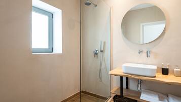 Un baño moderno con ducha envuelta en vidrio, un espejo grande y un tocador de madera con lavabo.