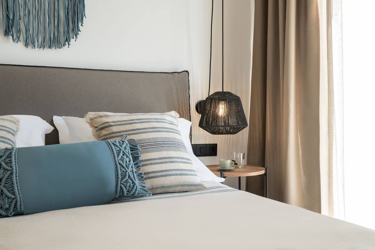 A neatly made bed with striped pillows and a blue throw blanket. A modern lamp is on a small table beside the bed.
