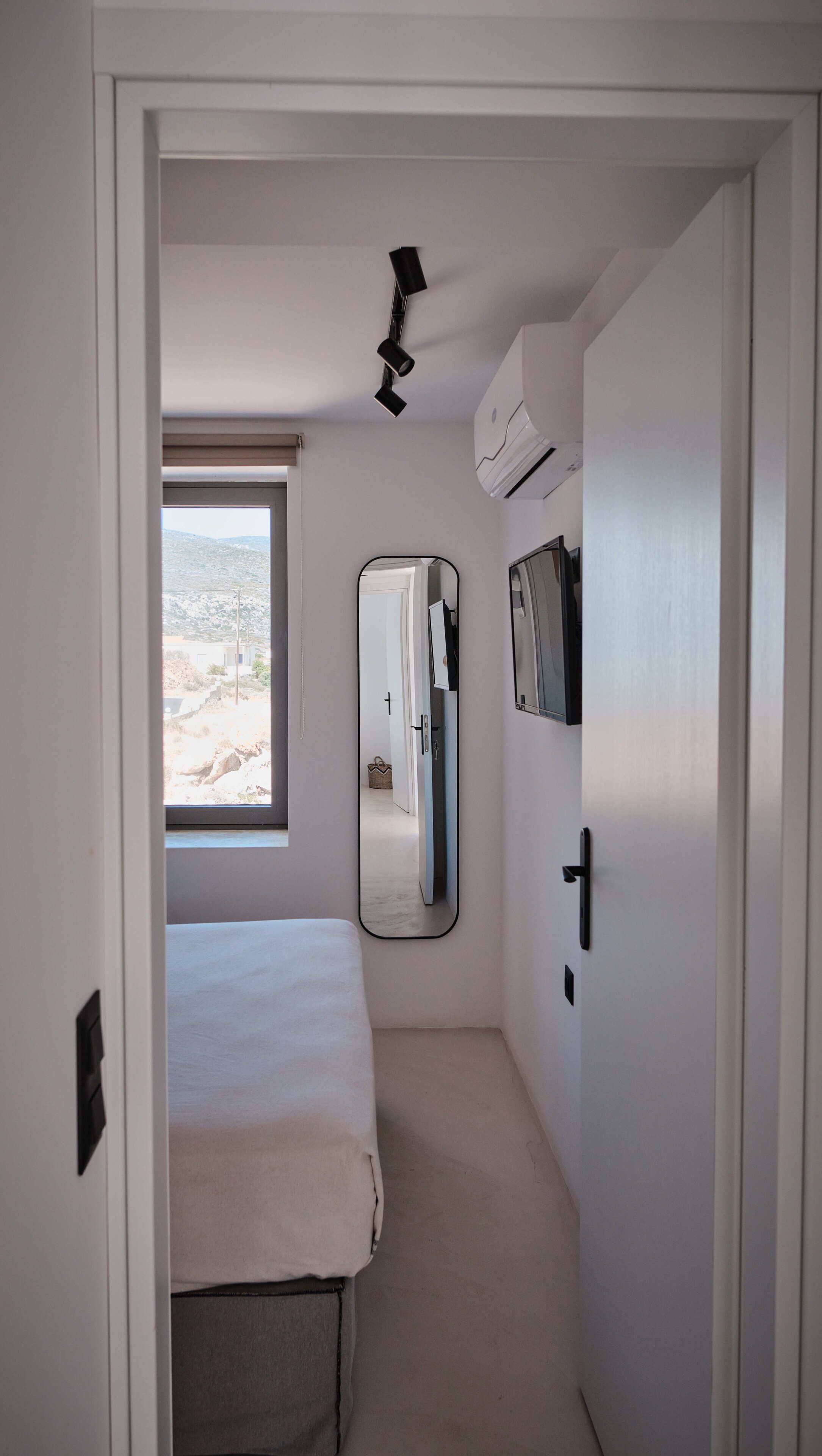 Una habitación pequeña con una cama, un espejo, un equipo de aire acondicionado y una ventana con vistas a un paisaje montañoso.