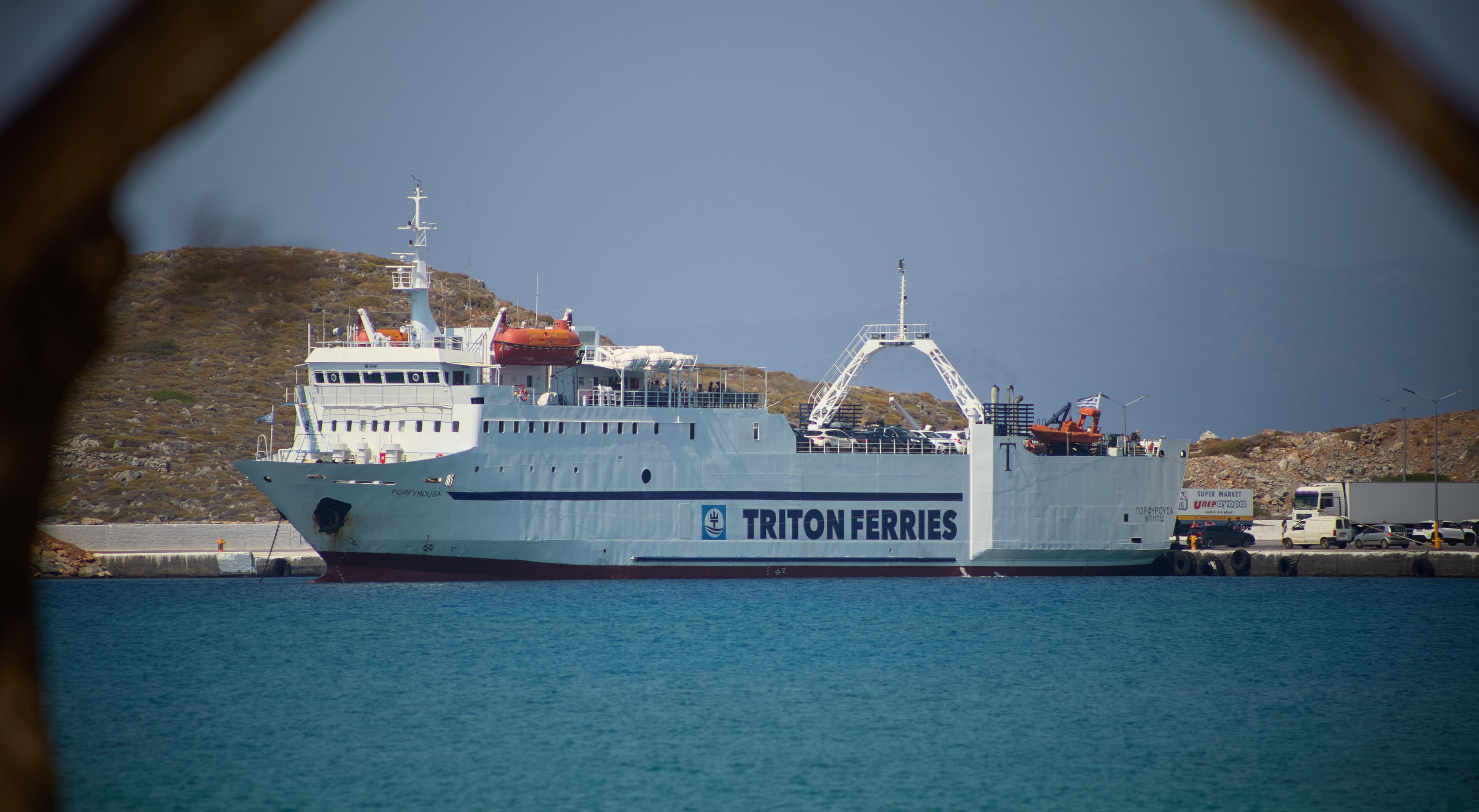 A ferry named 'TRITON FERRIES' docked at a port with a rocky landscape in the background.